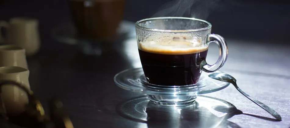 ถ้วยกาแฟดำในถ้วยแก้วใสบนจานรองพร้อมช้อน ทำไมกาแฟถึงมีคาเฟอีน