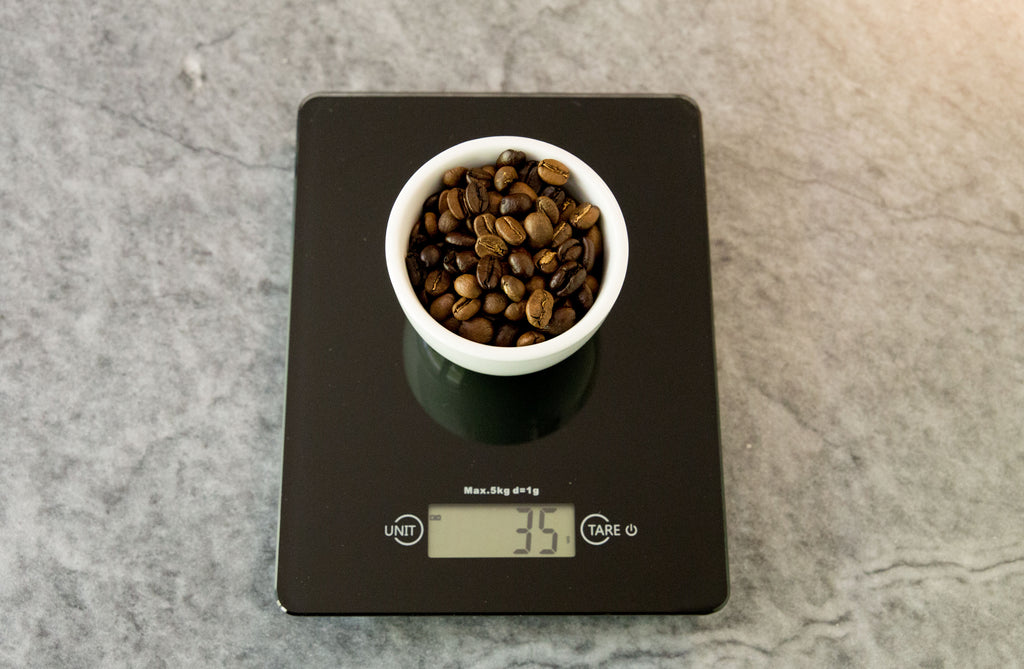 ชั่งน้ำหนักกาแฟ 35 กรัมในถ้วยสีขาวบนตาชั่งสีดำ